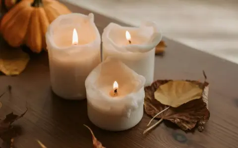 Candele accese su un tavolo di legno, con zucche e foglie autunnali. Un'ispirazione per chi vuole imparare come fare candele in casa.