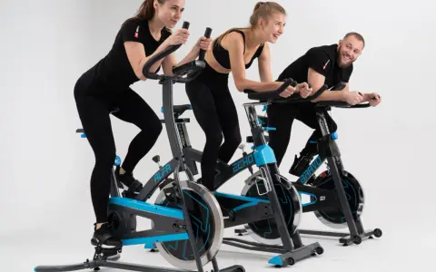 Trzy osoby ćwiczą na rowerach stacjonarnych. To świetny trening spinningowy!
