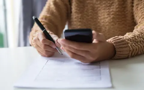 Kobieta z telefonem w dłoni wypełnia formularz, dokonując zgłoszenia darowizny online.