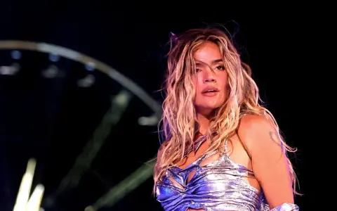 Karol G, con su melena rubia al viento, brilla en el escenario. Su atuendo plateado y el ambiente nocturno sugieren un concierto inolvidable de su gira.