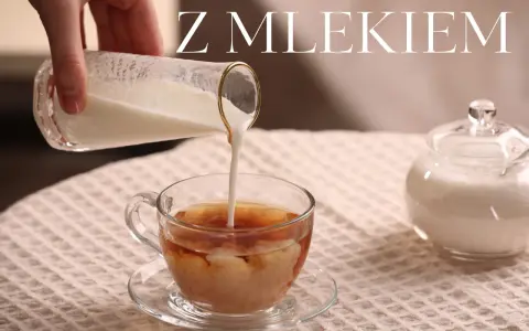 Ręka wlewa mleko do szklanki z herbatą, tworząc piękne smugi. Obok stoi cukiernica. Idealna herbata z mlekiem na chłodny dzień.