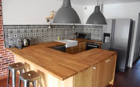 Cuisine moderne avec îlot central en bois, carrelage mural graphique et tabourets industriels. On dirait qu'on a réussi à faire une cuisine avec des vieux meubles revisités.