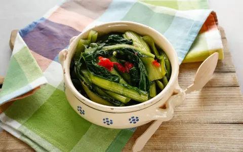 Cicoria in padella, un contorno saporito con peperoncino, servita in una ciotola decorata su un tagliere di legno.