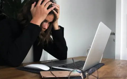 Kobieta z rękami na głowie przy laptopie, symbolizująca wypalenie i decyzję o porzuceniu pracy.