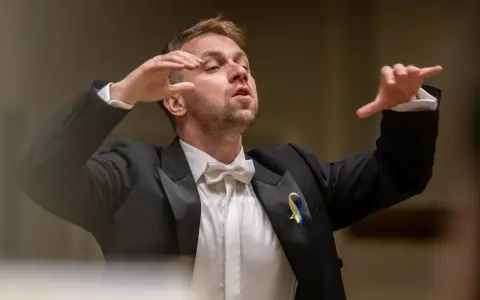 Dyrygent w garniturze z kokardką, prowadzący wykonanie Carmina Burana, z ukraińską wstążką na klapie.