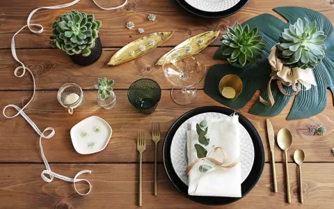 En vacker dukning med suckulenter, gyllene detaljer och gröna blad. En inbjudande och stilren bordsuppsättning.