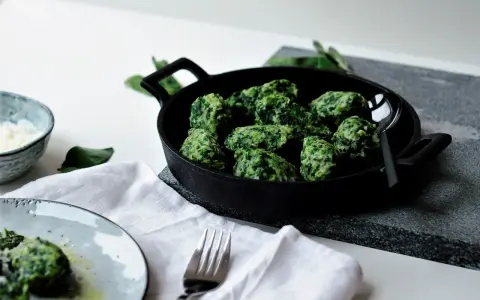 Malfatti, was ist das? Grüne, unregelmäßige Klößchen aus Spinat und Ricotta in einer Pfanne, daneben ein Teller mit mehr Malfatti und Parmesan.