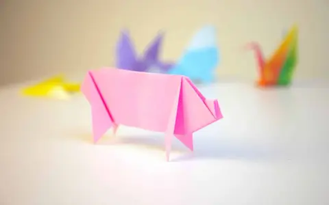 Cerdo de origami rosa con otras figuras de papiroflexia desenfocadas al fondo.