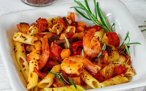 Penne-Nudeln mit Garnelen, Auberginen und Tomaten, garniert mit Rosmarin und Chiliflocken. Ein köstliches Gericht, das Lust auf mehr macht.