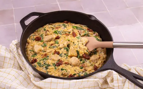 Un plat réconfortant de one pot orzo avec poulet, épinards et tomates séchées, servi dans une poêle en fonte.