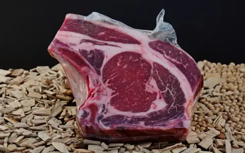 A vacuum-sealed raw beef steak with marbling sits on a bed of wood chips and small nuts.