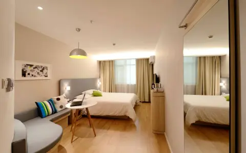 Habitación estrecha y alargada con cama, sofá curvo, mesa con portátil y espejo de cuerpo entero.
