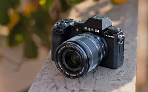 Czarny aparat Fujifilm X-S20 z obiektywem Fujinon leży na kamiennym murku.
