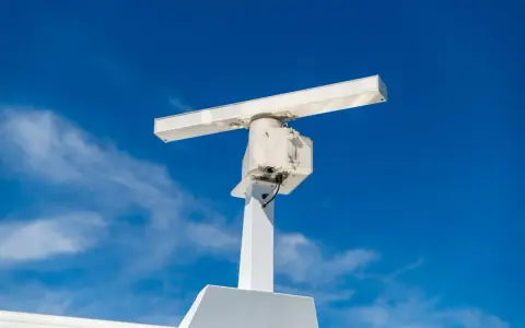 Antenne blanche sur un mât, sous un ciel bleu. Elle ressemble à un radar, mais pourrait aussi servir pour la communication satellite.