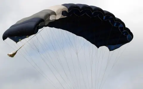 Ein großer, mehrfarbiger Fallschirm öffnet sich im Himmel, bereit für den Sprung aus dem Flugzeug.