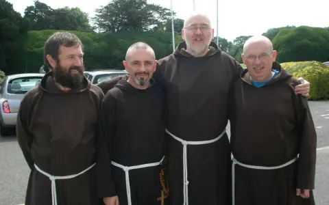 Four monk priests in brown robes stand together outdoors.