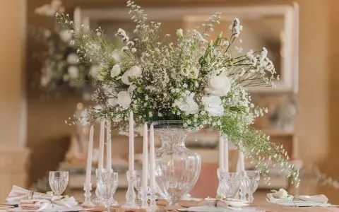 Un bouquet de vitrail fleur, blanc et aérien, orne une table dressée avec des bougies et des verres délicats.