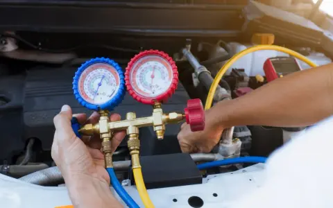 A mechanic uses a manifold gauge set to check for a freon leak in a car's AC system.