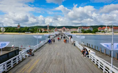 Spacer w Sopocie tętni życiem. Ludzie spacerują po drewnianym molo, podziwiając widok na plażę i zabytkowe budynki.