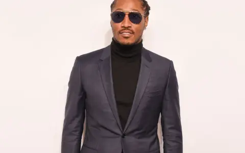 A man in a sharp black suit with a turtleneck, sporting stylish sunglasses.