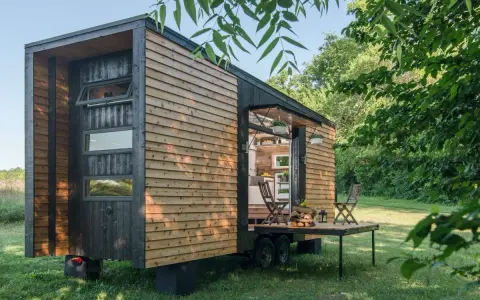Casa móvil de madera en un terreno no urbanizable, con mesa desplegable y sillas.