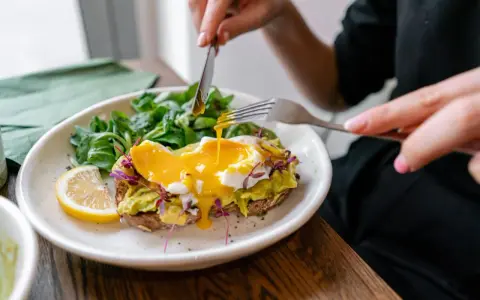 Tost z awokado i jajkiem sadzonym, polany żółtkiem, z sałatką i cytryną.