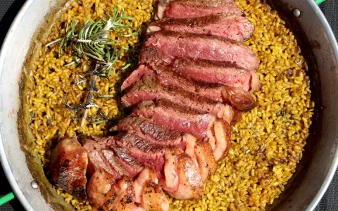 Arroz amarillo con chuletón a la parrilla y romero en paellera.