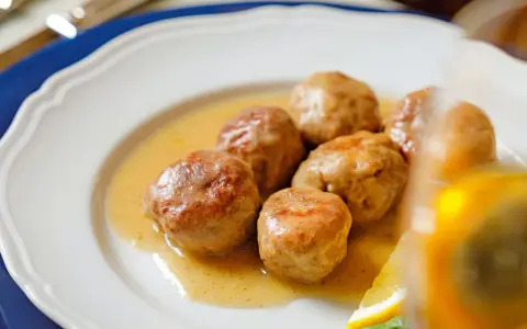 Polpette al limone succulente in un piatto bianco, con una fetta di limone e basilico.