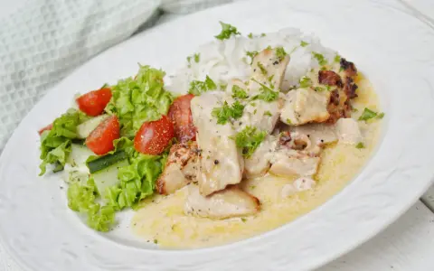 En krämig kycklinggryta med bacon, serverad med ris och en fräsch sallad.