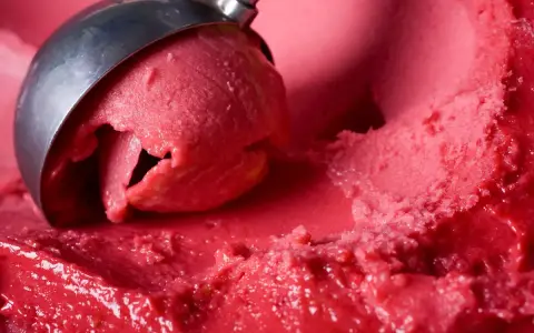 Ein Löffel nimmt eine Kugel leuchtend rotes Eis auf. Es sieht aus wie ein köstliches Blaubeereis, das zum Genießen bereit ist.