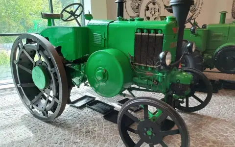 Zielony, zabytkowy Ursus, najstarszy model, z wielkimi kołami i kierownicą, stoi w muzeum.