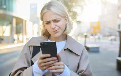 Zmarszczona kobieta patrzy na telefon, zastanawiając się, jak przestać zazdrościć innym.