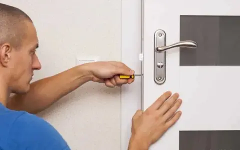 Un homme utilise un tournevis pour installer une serrure sur une porte de chambre.
