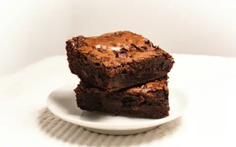 Dwa wilgotne ciasta brownie z płynną czekoladą, ułożone jedno na drugim na białym talerzyku.