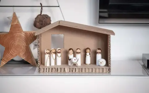Eine einfache Krippe basteln Kinder mit Holzfiguren und Karton. Maria, Josef und das Jesuskind sind in der Mitte, umgeben von Hirten und einem Schaf.