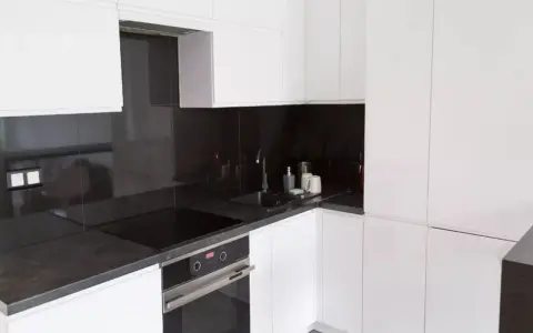 Nowoczesna, biała kuchnia z eleganckim, ciemnym blatem. Czarna płyta indukcyjna i zlew tworzą spójną całość.
