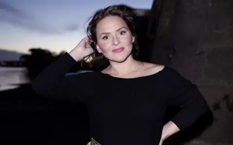 Emiliana Torrini, la chanteuse, pose au crépuscule près de l'eau, une main dans ses cheveux.