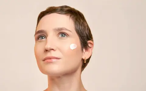 Une touche de crème solaire avant ou après crème hydratante sur la joue d'une femme au regard pensif.