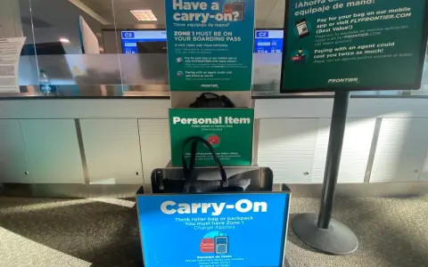 Frontier Airlines personal item size guide at the airport, showing a tote bag fitting in the "Personal Item" box and a roller bag in the "Carry-On" box.