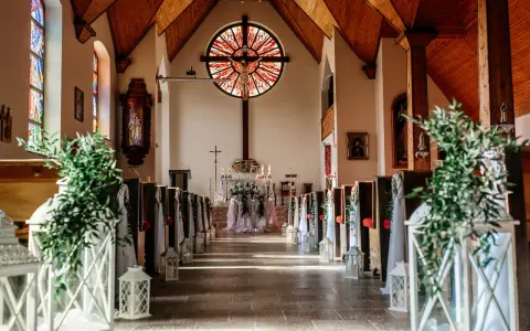 Piękna dekoracja kościoła na ślub samemu: lampiony, zielone gałązki i białe tkaniny tworzą romantyczną atmosferę.