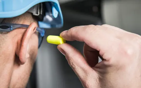 Main tenant, casque bleu, lunettes de protection et bouchon d'oreille jaune pour se protéger d'un bruit de 120 décibels équivalent.