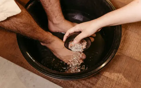 A hand pours pink salt into a foot bath, adding to the foot detox ingredients for a relaxing soak.
