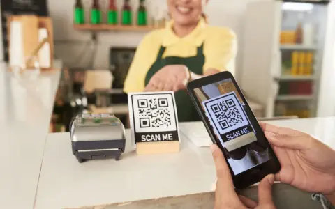 Cliente usa su móvil para escanear un código QR y hacer su carta digital. Un datáfono y otro código QR esperan en el mostrador.
