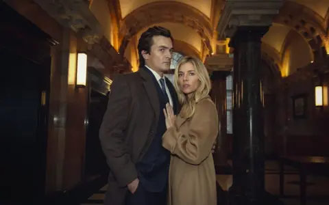 Coppia elegante in un corridoio sontuoso, forse il finale dell'anatomia di uno scandalo trama.