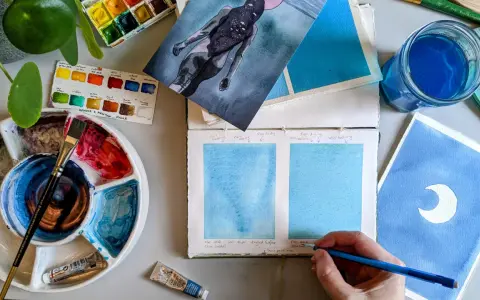 Paleta de acuarelas, pinceles y muestras de pintura azul. Un artista experimenta con técnicas de pintar acuarela.