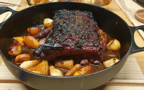Poitrine de porc rôtie, croustillante et savoureuse, servie avec des pommes de terre et des carottes dans une cocotte en fonte.