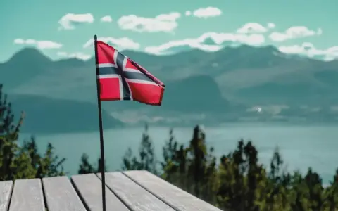 Norweska flaga na tle gór i jeziora. Pomyśl o tym, jak wysłać zwolnienie lekarskie do NAV, gdy jesteś w tak pięknych okolicznościach.