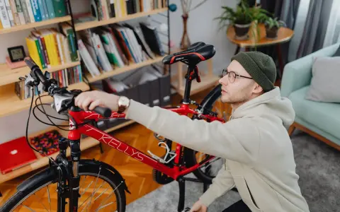 Mężczyzna przygotowuje rower do wysyłki w całości. W tle regał z książkami i rośliny.