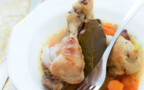 Delicioso pollo guisado con zanahorias y hoja de laurel en un plato blanco, listo para ser disfrutado.