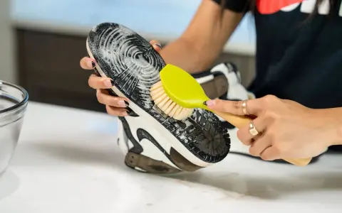 Mani che puliscono la suola di una scarpa con una spazzola gialla e schiuma. Un modo efficace per capire come pulire la suola delle scarpe.